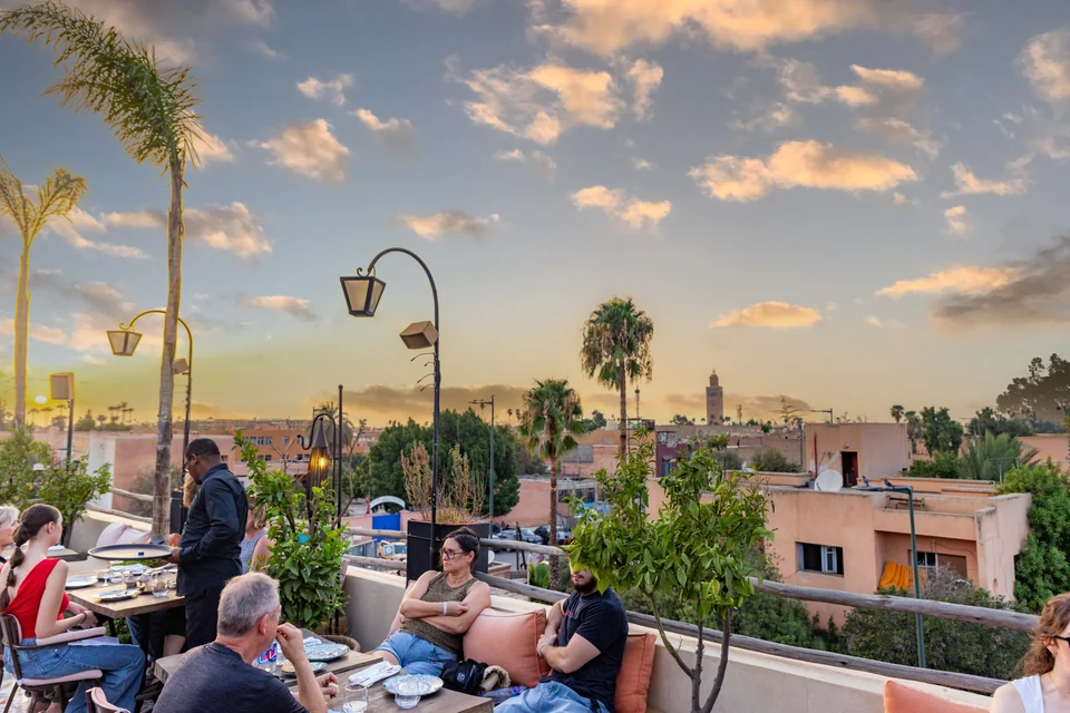 Comensales en la terraza Coco Rooftop con la Koutoubia y el cielo vespertino