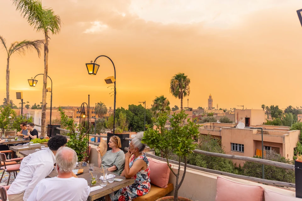 Clientes cenando junto a las plantas de la terraza con la Koutoubia al atardecer